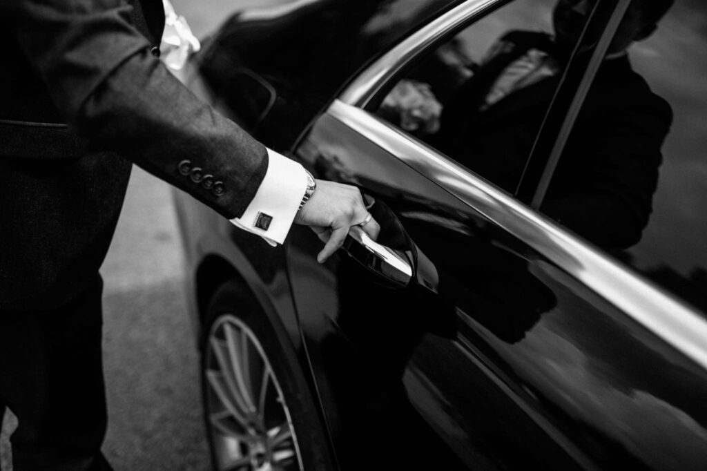 Photo noir et blanc d'un chauffeur ouvrant une portière de voiture en plan rapproché, on ne voit que la main sur la poignée