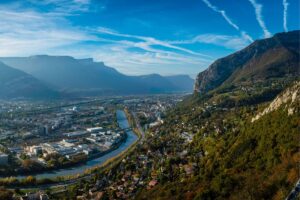 Vue aérienne lointaine et verdoyante de Grenoble illustrant les avantages écologiques de la ville